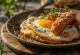 Saucisse Alheira servie avec un œuf au plat, parsemée de persil, sur une assiette rustique