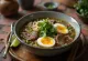 Pho au bœuf et aux œufs servi dans un bol avec des œufs, du bœuf et des nouilles de riz, de la coriandre fraîche et des tranches de citron vert