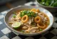 Hủ tiếu au poulet, servi avec de la coriandre fraîche et de l'oignon vert, riche bouillon